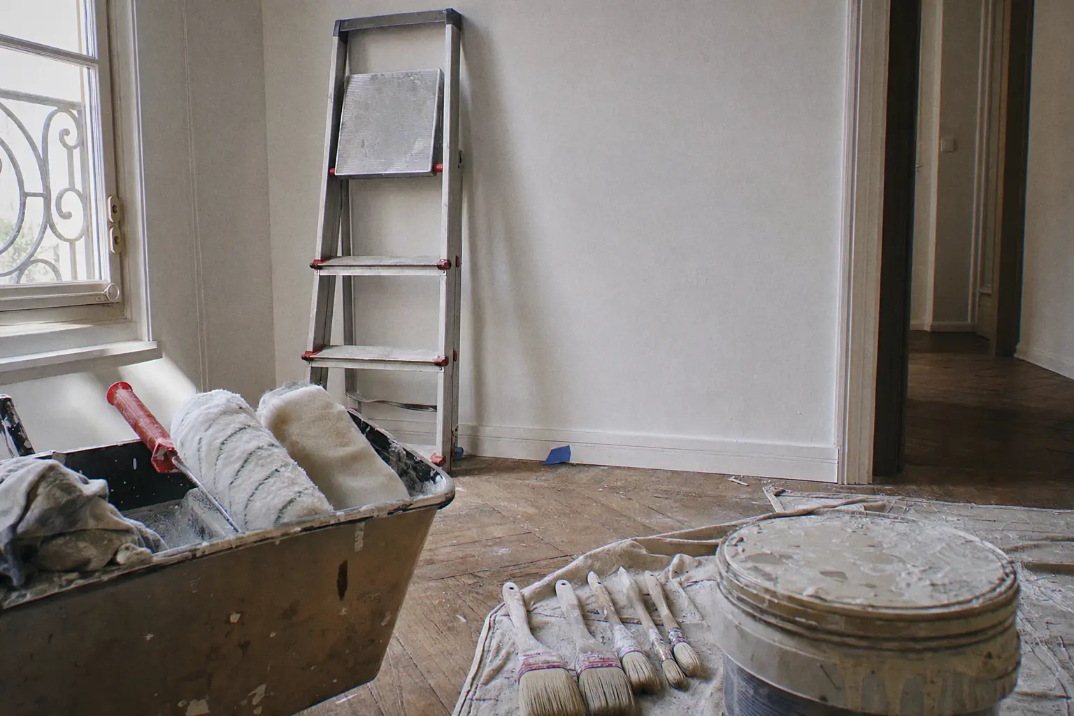 End of the day on site: rollers in the tray, cleaned brushes on a dust sheet, folded stepladder against a freshly painted wall