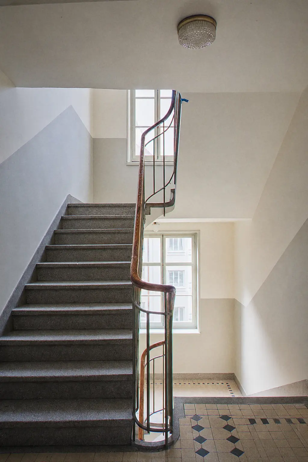Geneva apartment-building stairwell repainted in two tones, wooden handrail, granite steps