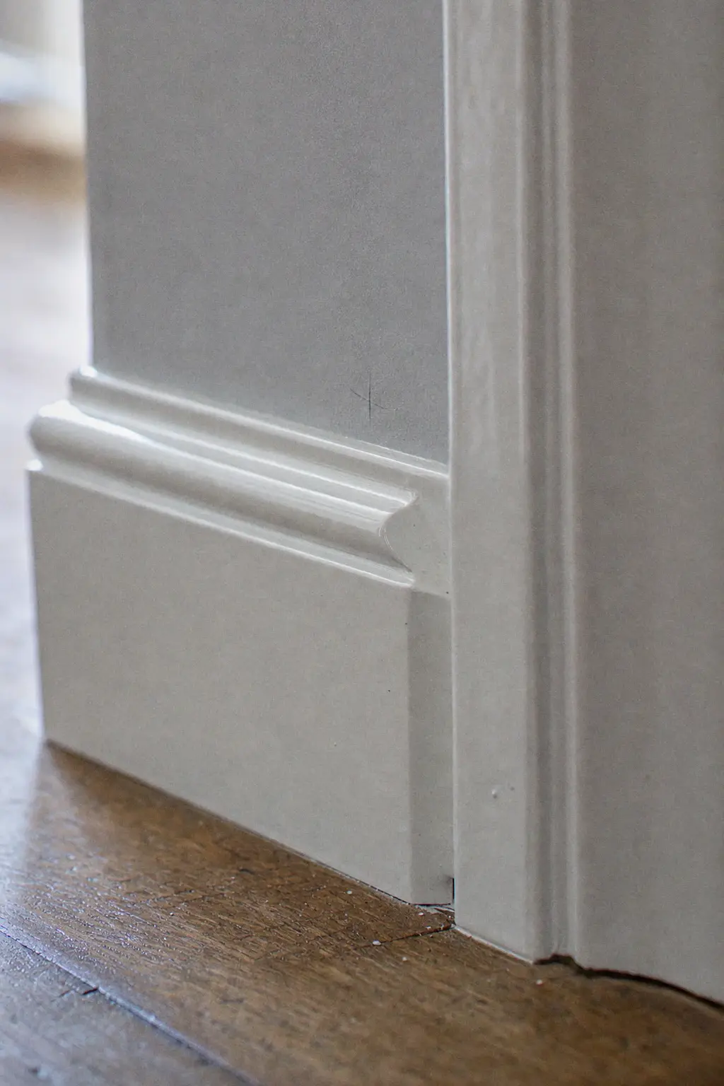Skirting board and door frame in satin white enamel, crisp edge against the light-grey wall